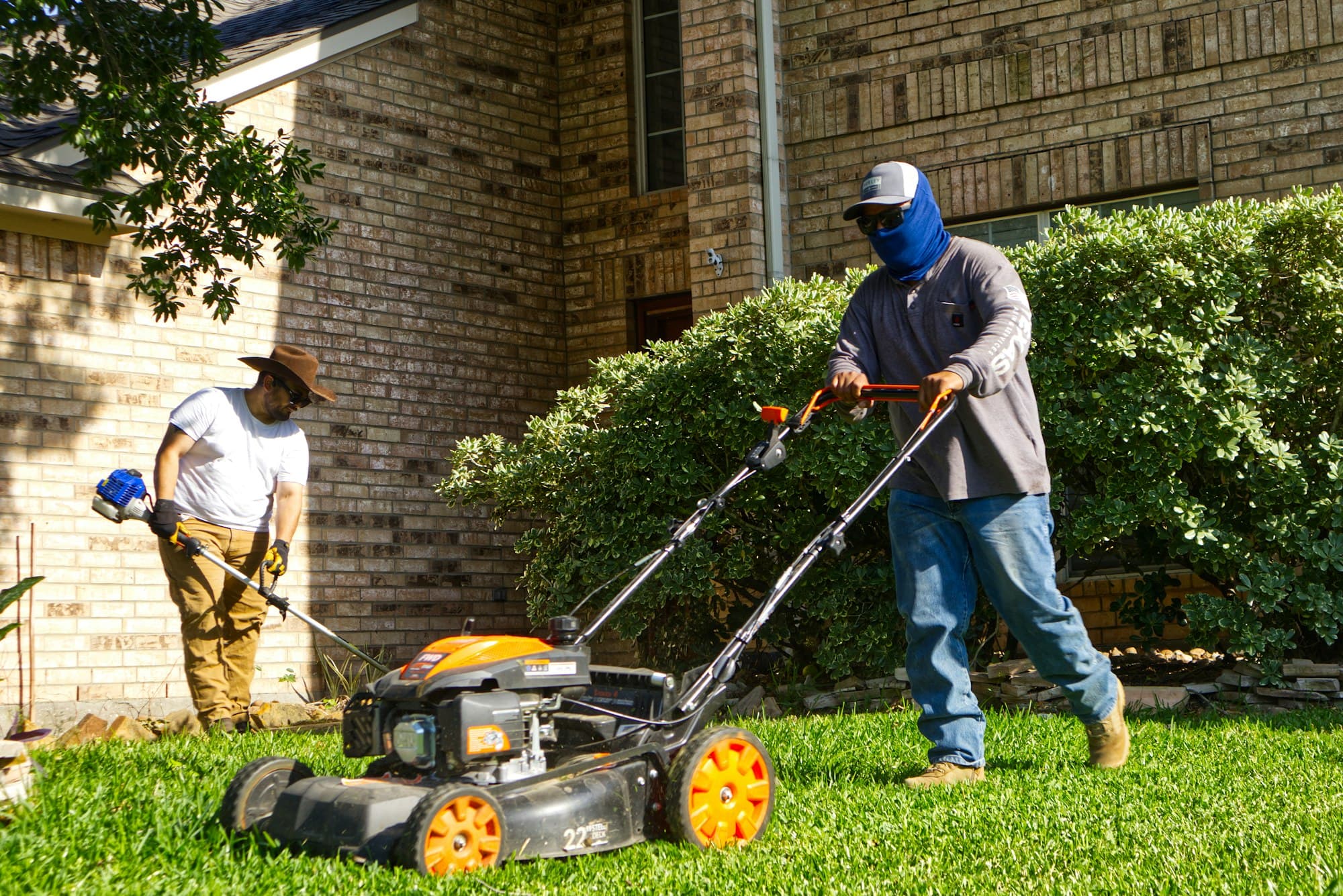 Two landscapers mowing and trimming a front lawn